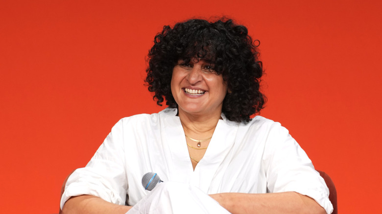 Samin Nosrat wearing white and speaking at a panel with a red background