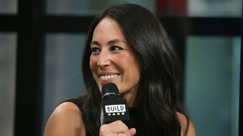 Joanna Gaines looking to the side and smiling while holding a microphone.