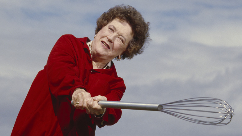 Julia Child wearing red, swinging a giant whisk.