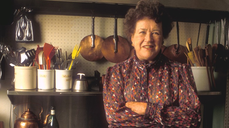 Julia Child standing in her kitchen with arms crossed.