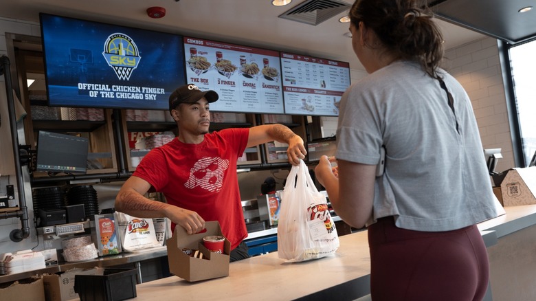 A person ordering food from a cashier at the Raising Cane's counter