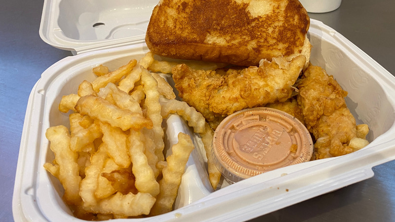 A container of chicken, fries, and toast with a dipping sauce