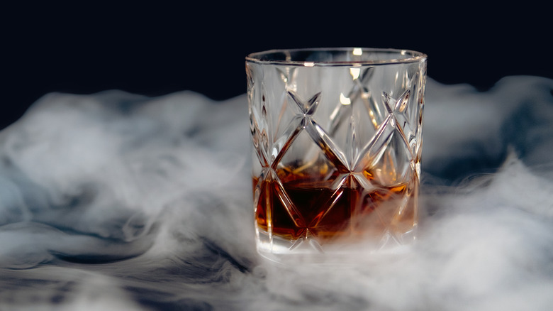Glass of whisky surrounded by smoke against a dark background