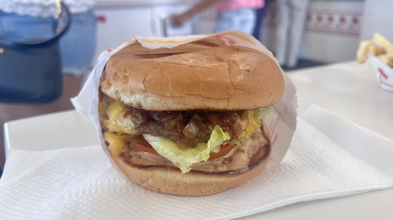 In-N-Out cheeseburger on a napkin served inside a restaurant with cheese, onions, and lettuce showing on the side