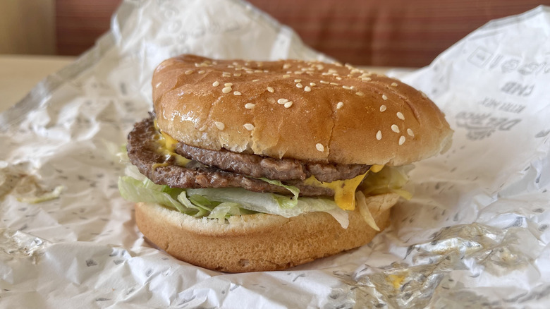Side close-up image of Del Taco Double Del Cheeseburger with a paper wrapper