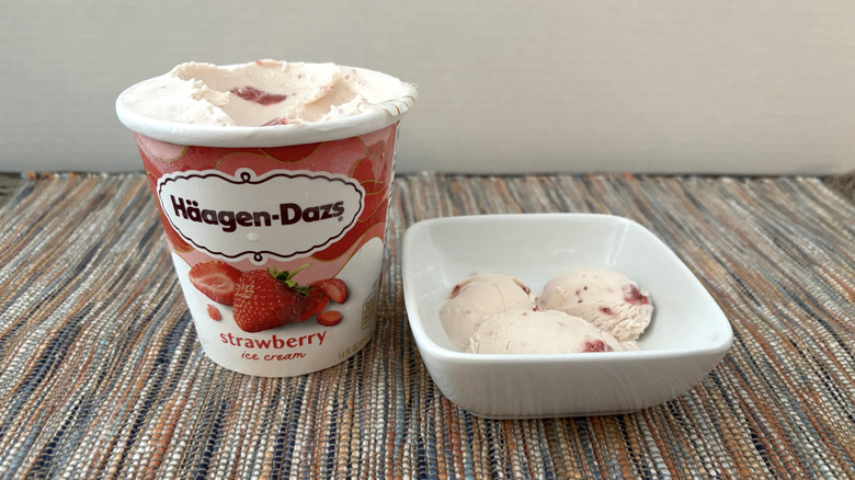 Häagen-Dazs strawberry ice cream in carton and bowl on neutral placemat