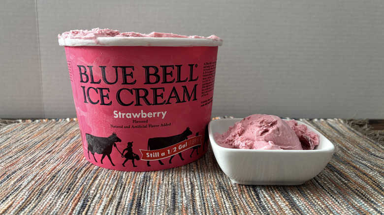 Blue Bell strawberry ice cream in carton and bowl on neutral placemat