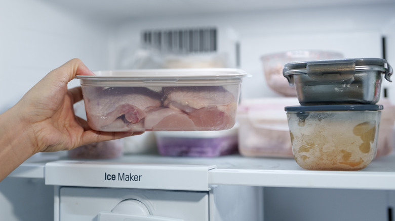 A person places a plastic container with raw chicken into the fridge