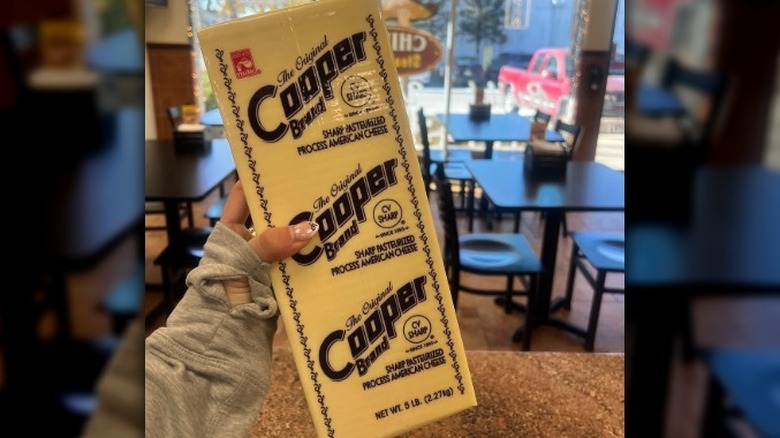 Person holding Cooper Brand White Sharp American cheese package