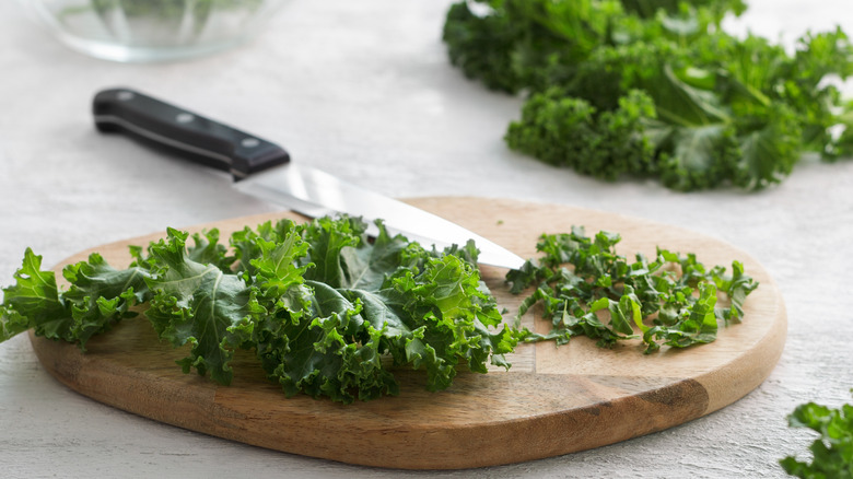 Leaves of kale on a wooden cutting board next to a knife.