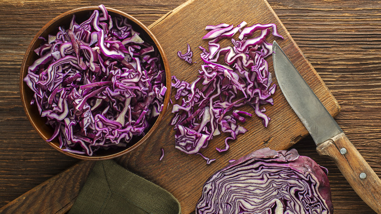 bowl of shredded red cabbage plus a board with more cabbage, a knife, and a half cabbage