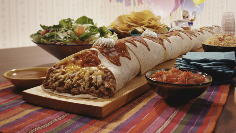 giant burrito on plate with salsa, salad, and chips
