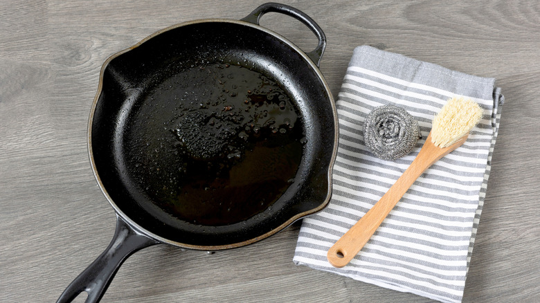 Dirty cast iron pan next to a towel, steel wool and brush