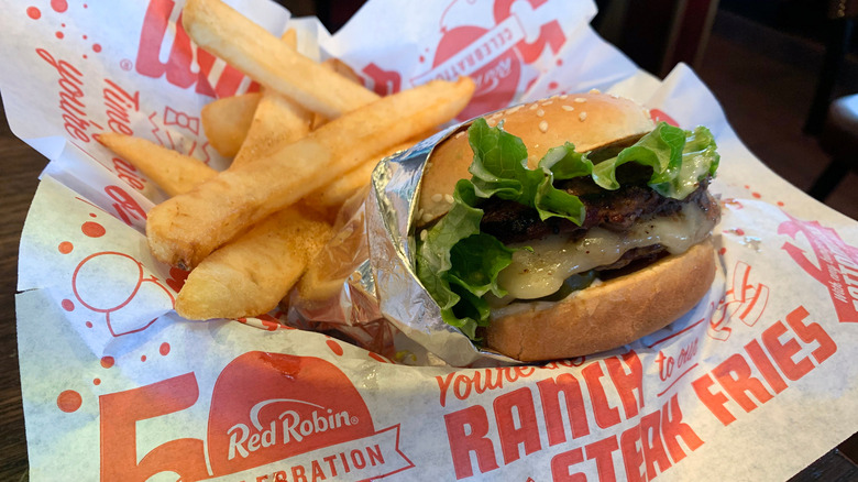 A Red Robin burger and steak fries, resting on greaseproof paper branded with the company logo