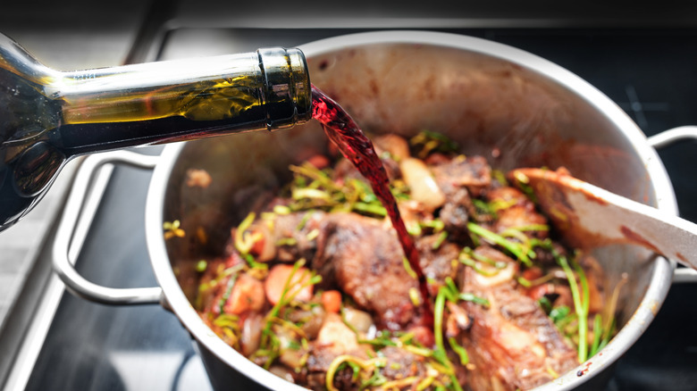 Red wine being poured into a pot of beef and herbs to deglaze the pan