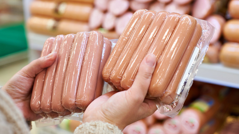 Hands holding up two packages of hot dogs in a store