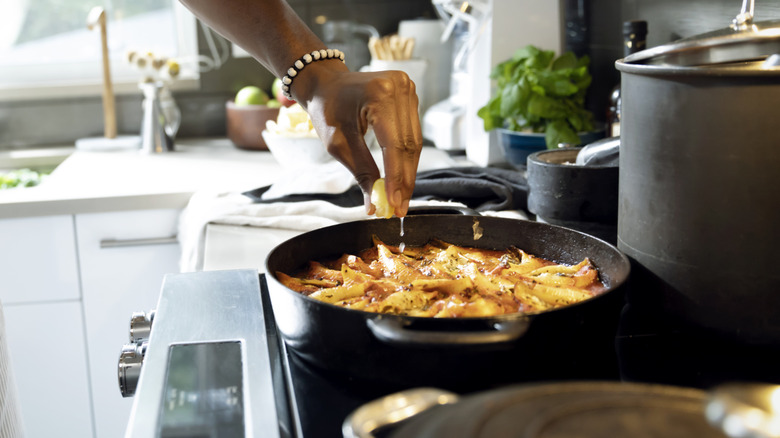 person squeezing half a lemon into a pan of food on the stove