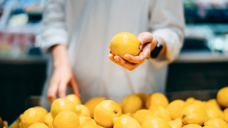 person holding a lemon above a lemon display in a grocery store