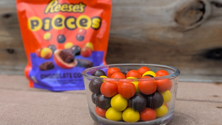 Reese's Pieces Chocolate Cookie candy pieces in a glass bowl with the bag of candy in the background