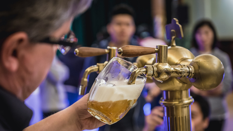 A person pouring a frothy beer from and ornate beer tap
