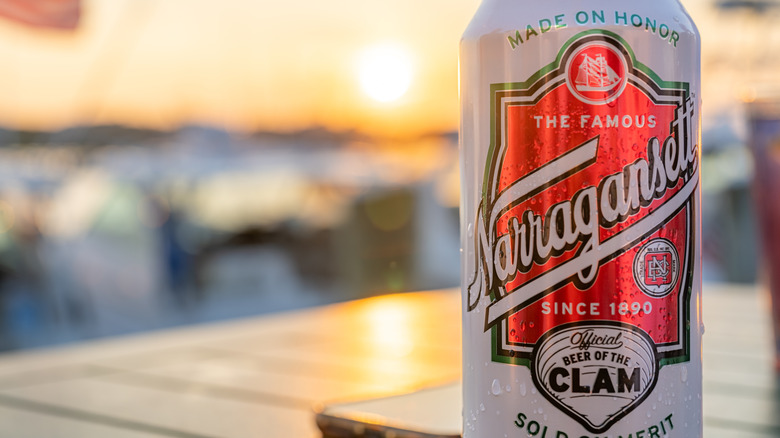 A close shot of a can of Narragansett in front of a blurred marina at sunset