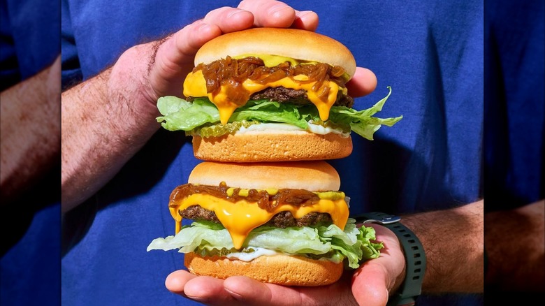 Two hands holding two stacked cheeseburgers