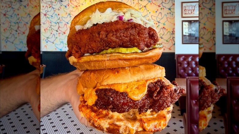 Hand holding two hot chicken sandwiches inside restaurant