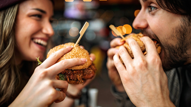 Two smiling people eating Nashville hot chicken sandwiches