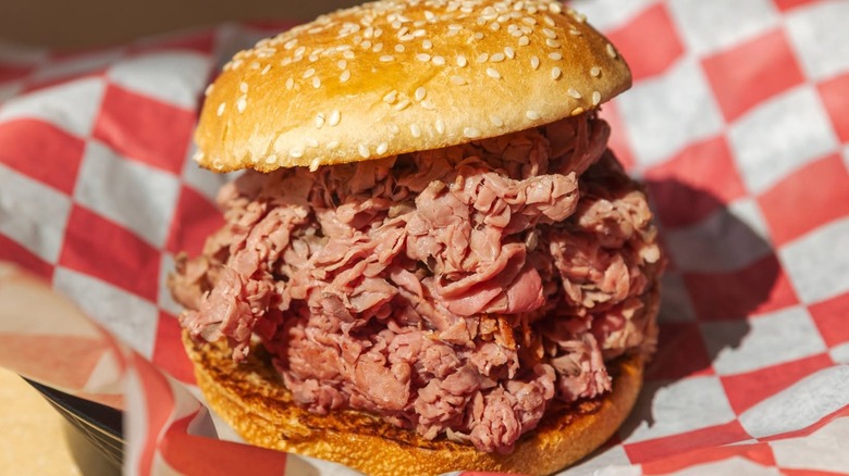 Roast beef sandwich on sesame seed bun on red and white paper
