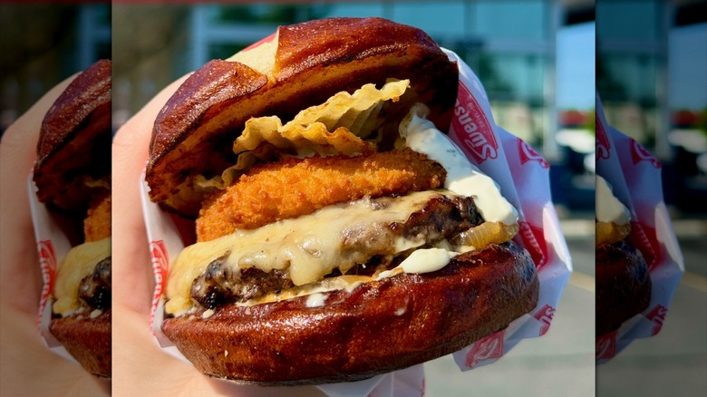 Hand holding burger on pretzel bun outside