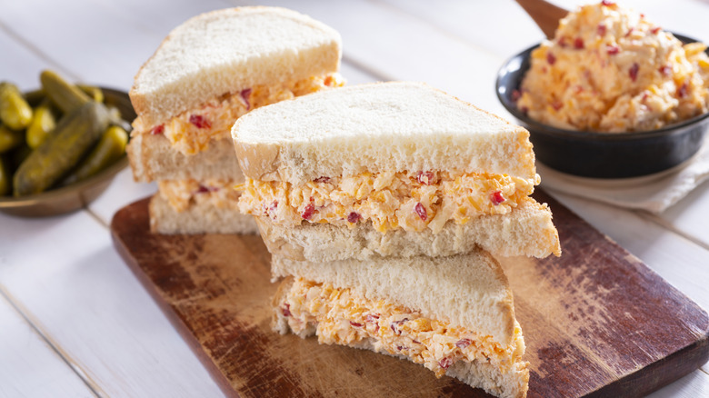 Sliced pimento cheese sandwiches with pickles and bowl of pimento cheese