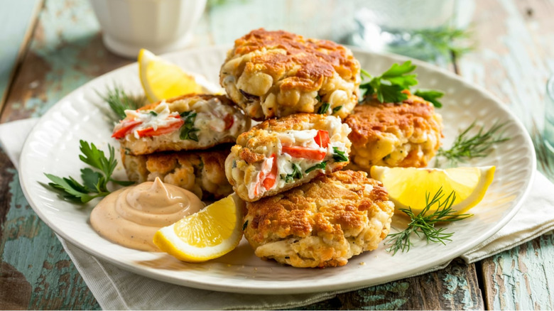Crab cakes served on white plate with dill, aioli, and lemon wedges