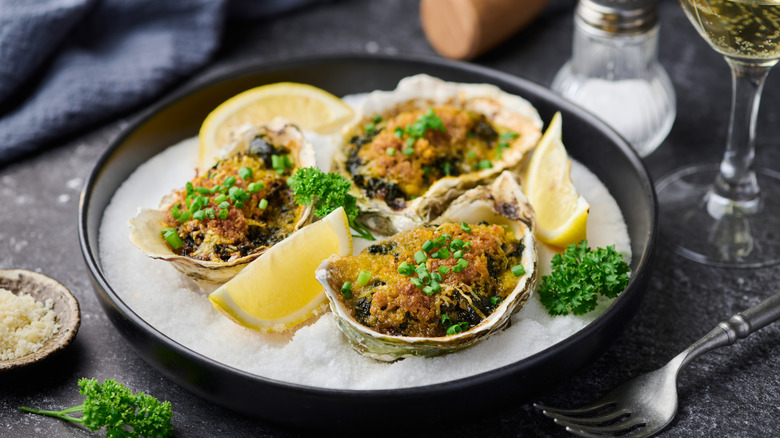 Oysters Rockefeller served in bowl of ice with lemon wedges
