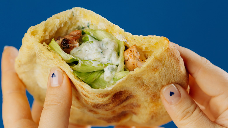 A person holding a pita wrap filled with chicken, lettuce, and sauce