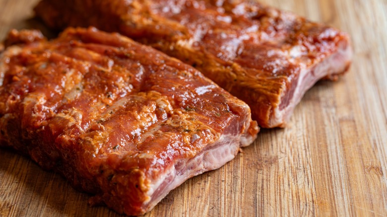 Raw pork ribs, cut in half and glistening with a marinade, on a cutting board