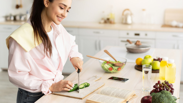 woman following a recipe while cutting cucumbers