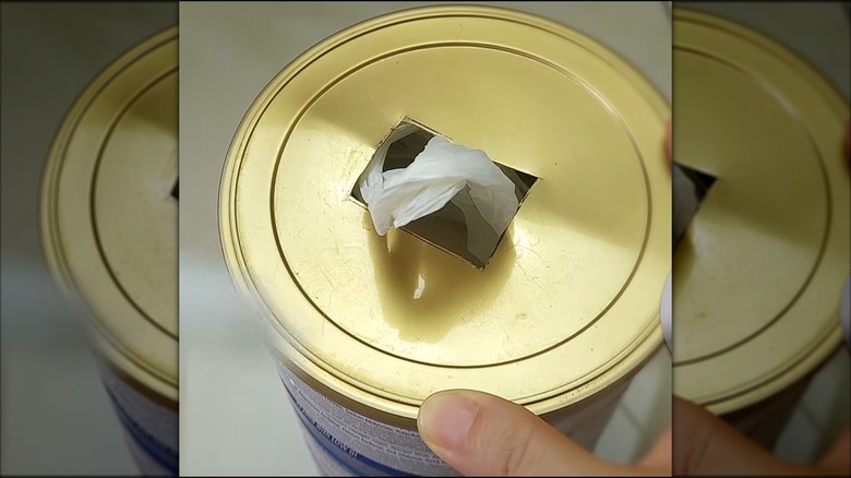 Hand holding can with plastic bag coming through lid