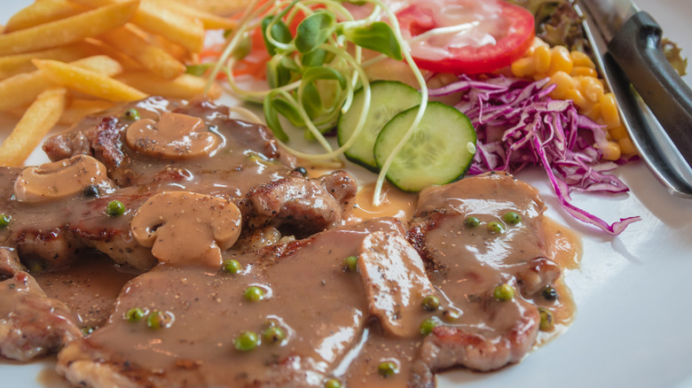 steak smothered in mushrooms sauce with fries and salad