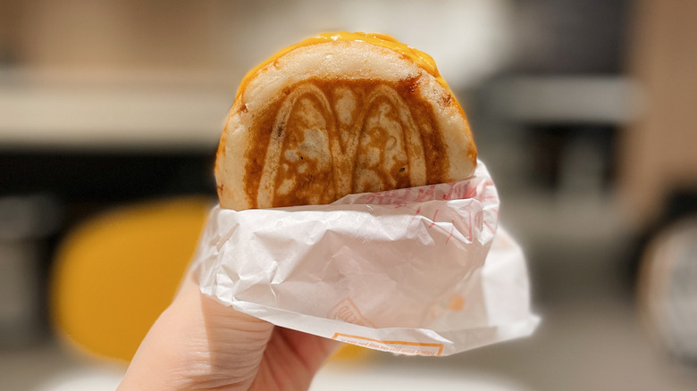 Hand holding a partially wrapped McDonald's McGriddle sandwich