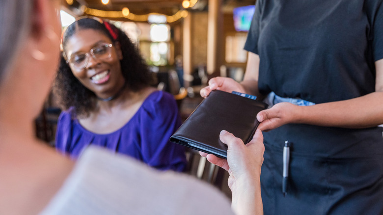 A restaurant diner hands a server the bill holder with their credit card sticking out.