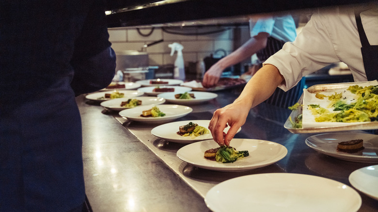 The hands of a chef plating multiple dishes in a restaurant kitchen