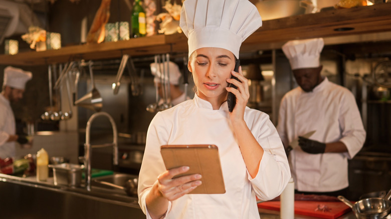 Female chef on the phone while holding tablet.