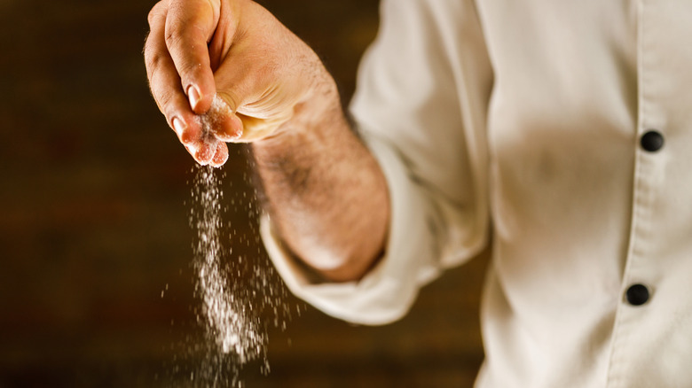 A male chef's hand sprinkling salt.