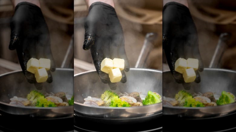 A gloved hand adding butter to vegetables.