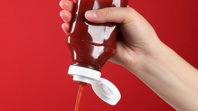 hand squeezing unlabled bottle of ketchup over bright red backgorund