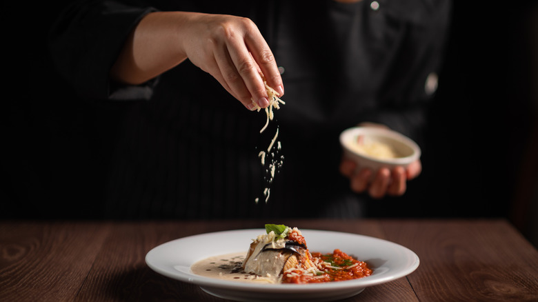 Chef sprinkles shredded cheese on plated dish