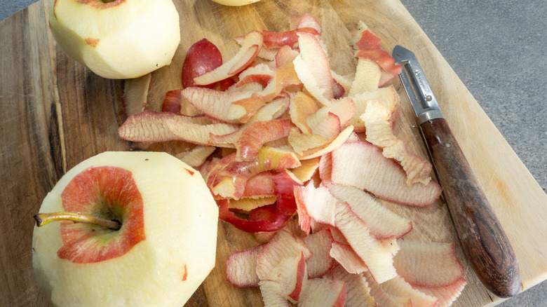 Apple peels sit on a wooden cutting board next to peeled apples.