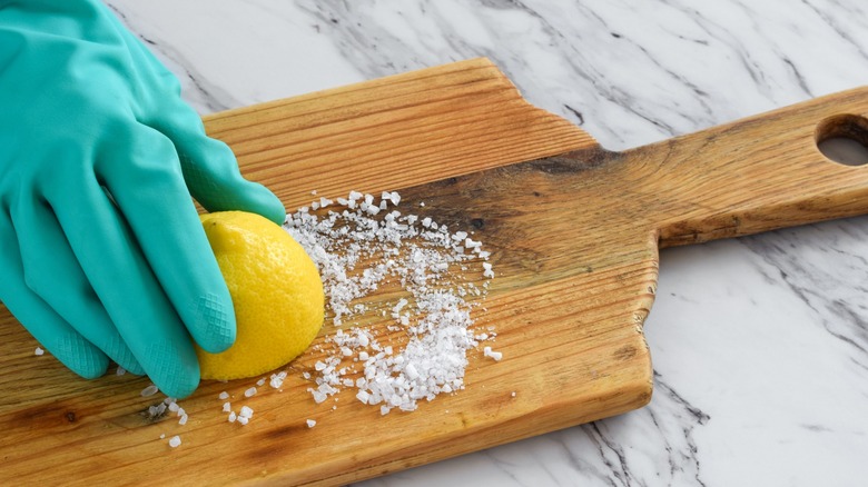 Gloved hand scrubbing salt and lemon on a wooden cutting board
