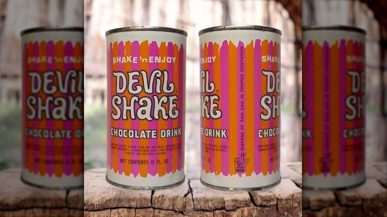 Two old cans of Devils Shake with a retro orange and a fuchsia stripe design. The label says shake n' enjoy Devil Shake chocolate drink