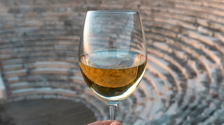 Hand holding a glass of white wine in an amphitheater